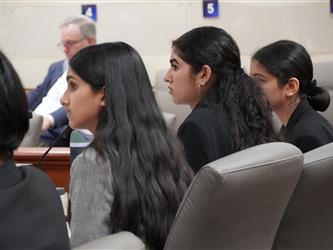 Student participants review notes and monitor proceedings from counsel table during a mock trial competition.